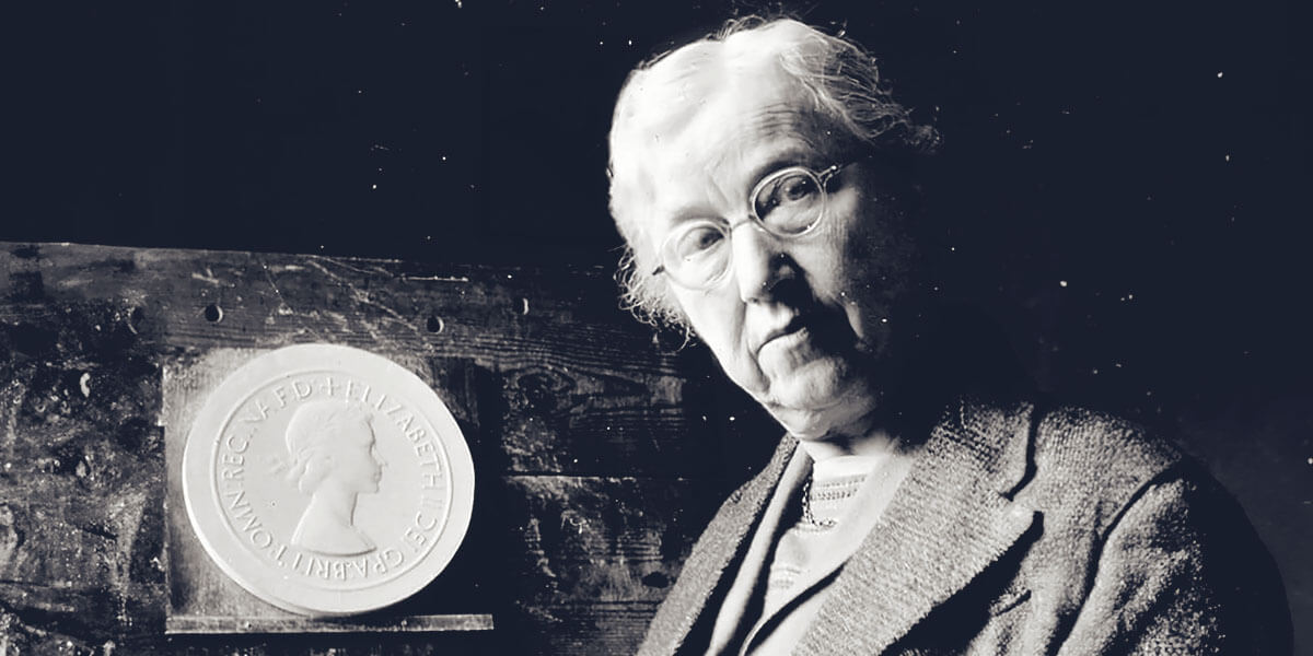 A black and whit photograph of Mary Gillick posing next to a plaster cast of her definitive Queen Elizabeth II portrait